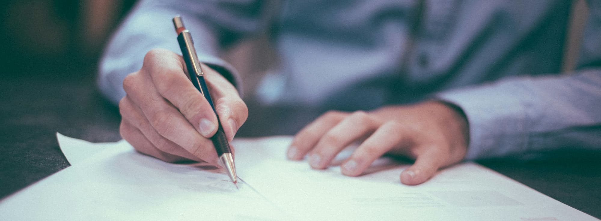 Eine Hand unterschreibt ein Dokument mit einem Stift